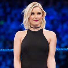 a woman with blonde hair wearing a halter top and black pants standing in front of a blue ring