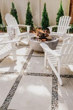 two white adiron chairs sitting on top of a patio next to a fire pit