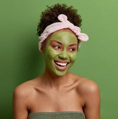 a woman with green facial mask on her face and towel around her head, smiling at the camera