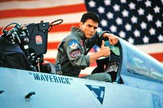 a man sitting in the cockpit of a fighter jet pointing at an american flag behind him