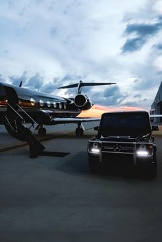 a black truck parked next to an airplane on the tarmac at dusk with a plane in the background