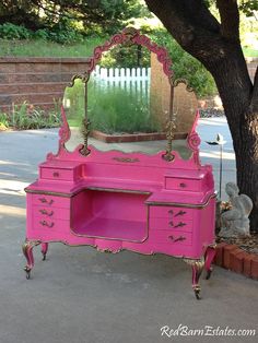 a pink vanity with an ornate mirror on it's top and drawers underneath a tree