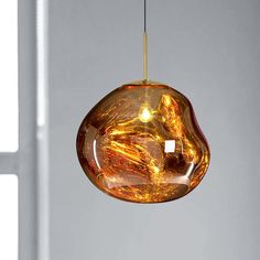 a glass light hanging from a ceiling in front of a white wall with a window