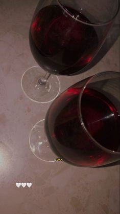 two glasses of red wine are sitting on a table with hearts drawn on the glass