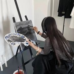 a woman sitting in front of an easel painting on a piece of paper and wearing headphones