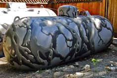 a large gray tank sitting on top of a gravel field next to a wooden fence