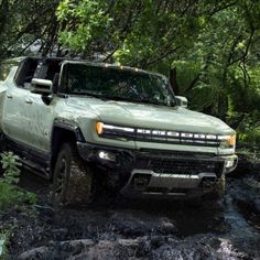 a green truck driving through some water in the woods