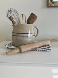 kitchen utensils are sitting in a mug on a counter top next to a whisk and rolling pin