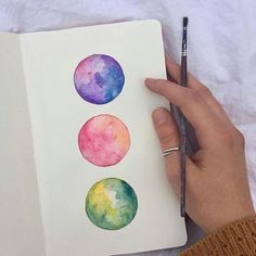 a person is holding a pencil and drawing with watercolors