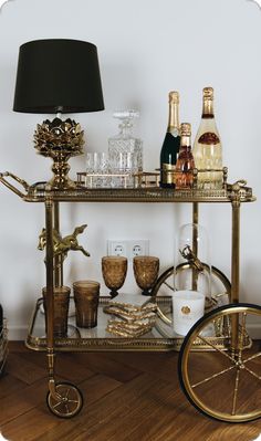 a gold bar cart filled with liquor bottles and glasses on top of a hard wood floor