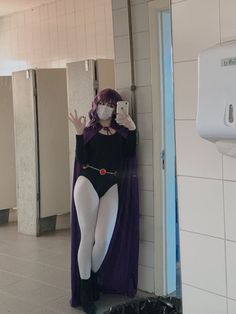 a woman dressed in costume taking a selfie with her cell phone while standing next to a urinal