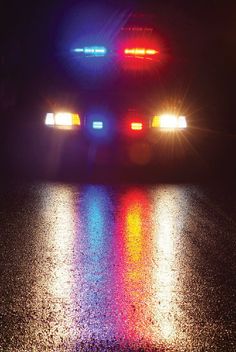 a police car with its lights on is parked in the rain and reflecting off the wet pavement