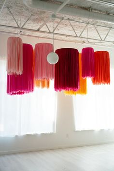 several different colored lights hanging from the ceiling in an empty room with white walls and windows