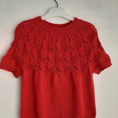 a red sweater hanging on a hanger next to a white wall with an openwork design