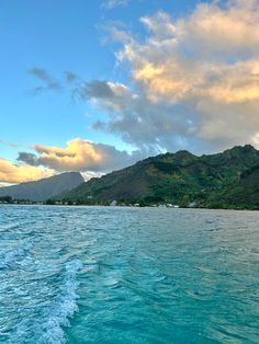 the water is crystal blue and there are clouds in the sky over mountains behind it