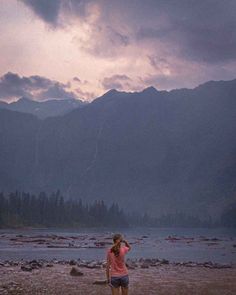 a woman standing on top of a sandy beach next to a lake under a cloudy sky