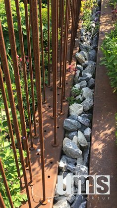 there is a rock wall in the middle of this garden with metal poles and flowers