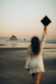 a woman in white dress holding up a black square object over her head at the beach