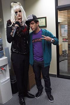 two people standing next to each other in an office area with one pointing at the camera