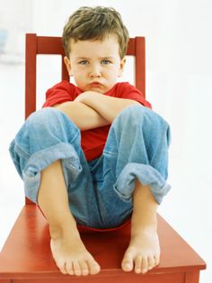 a young boy sitting on top of a red chair with his legs crossed in front of him