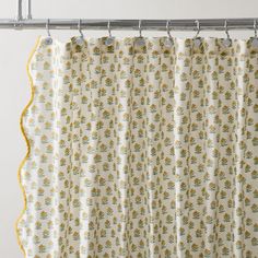 a shower curtain with yellow and white floral print on it, hanging from a metal rod