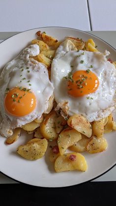 two fried eggs and potatoes on a white plate