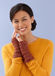 a smiling woman in yellow sweater holding her hand on her face and wearing knitted mitts