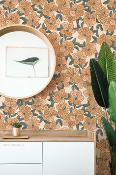 a mirror on the wall next to a plant in a room with floral wallpaper