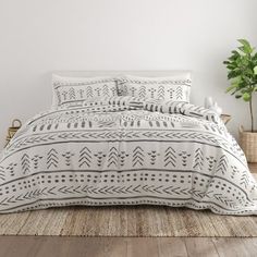 a bed with white and black patterned comforter set on top of a wooden floor next to a potted plant