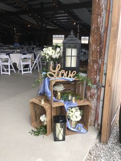 an arrangement of wooden crates with flowers and candles on them in front of a barn