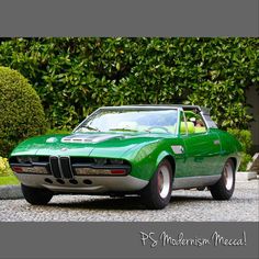 a green sports car parked in front of a hedge