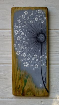 a dandelion painted on a wooden plaque with white flowers in the center, against a white wall