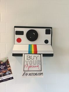 a polaroid camera mounted to the side of a white wall next to a book