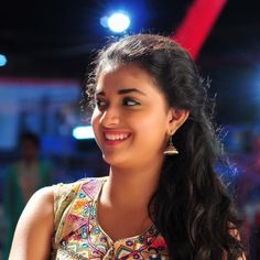 a woman with long black hair smiling at the camera while wearing a colorful top and earrings