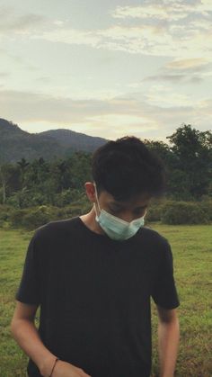 a young man wearing a face mask while standing in a field with mountains in the background