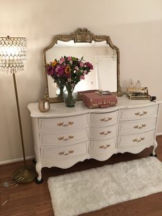 a white dresser with flowers and a mirror