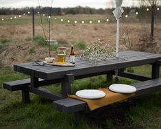 a picnic table with plates and drinks on it in the middle of a grassy field