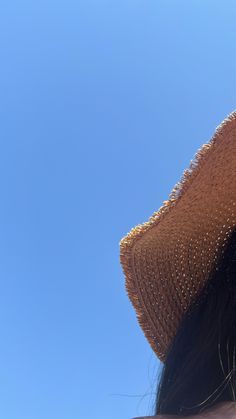 the back of a woman's head wearing a brown straw hat and blue sky