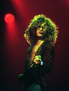 a man with long hair holding a microphone in his right hand and standing on stage