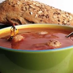 a green bowl filled with soup next to bread and tomatoes