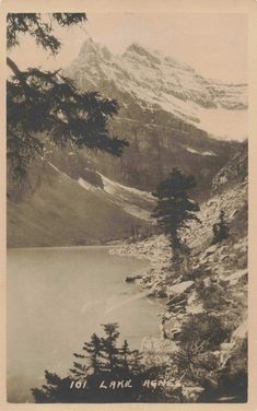 an old black and white photo of a mountain lake with trees in the foreground