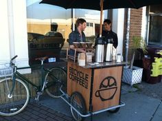 two men standing at a coffee cart with an umbrella