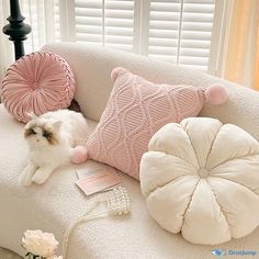 a white cat sitting on top of a couch next to two pillows and a phone