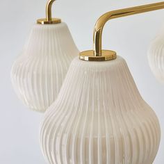 three white glass lamps hanging from a gold metal arm