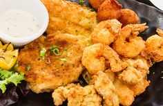 a black plate topped with fried food next to a bowl of ranch dressing and salad