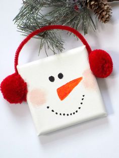 a snowman ornament hanging from a christmas tree with red pom - poms