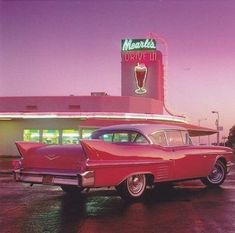 an old red car is parked in front of a drive - by restaurant at dusk