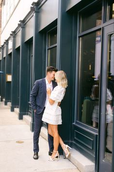 a man and woman standing next to each other in front of a store window kissing