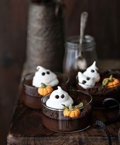 three small desserts with white frosting and pumpkins in them on a wooden table