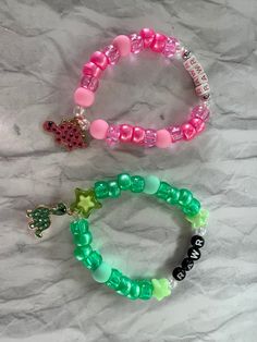 two bracelets with charms on them sitting on a white tablecloth covered surface, one is green and the other is pink